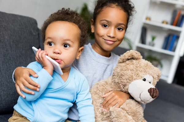 Frères et sœurs avec smartphone et ours en peluche — Photo