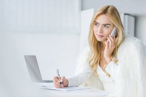 Businesswoman writing and talking on smartphone — Stock Photo, Image