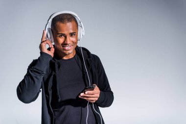 Genç Afro-Amerikan adam akıllı telefon kullanarak ve gri izole kamera gülümseyen kulaklık 