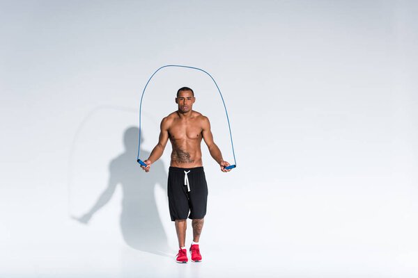 shirtless african american sportsman exercising with skipping rope on grey