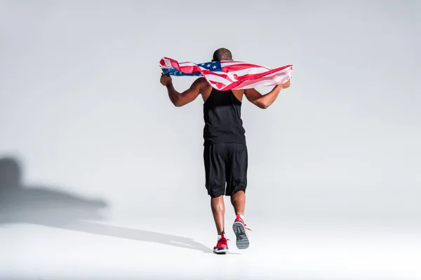 グレーにアメリカの国旗を保持している若いアフリカ系アメリカ人のスポーツマンの背面図 — ストック写真
