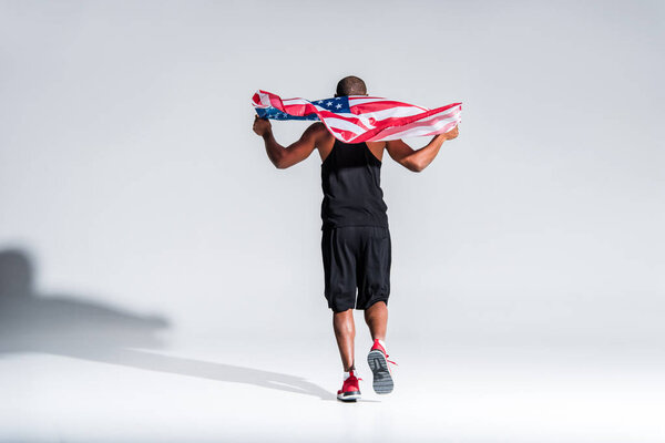 back view of young african american sportsman holding american flag on grey
