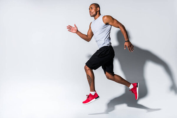 athletic young african american sportsman running on grey