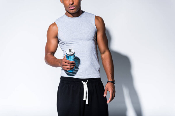 cropped shot of young african american sportsman holding sports bottle with water on grey