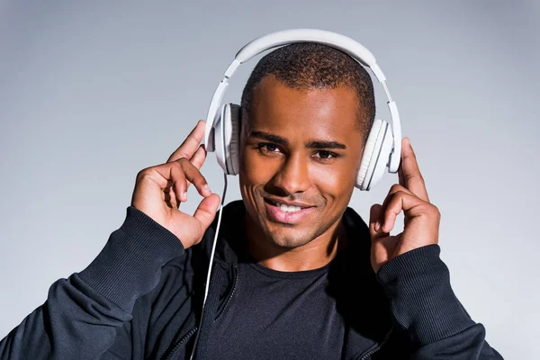 ハンサムな若いアフリカ系アメリカ人スポーツマンのヘッドフォンで音楽を聴く グレーに分離カメラで笑顔 — ストック写真