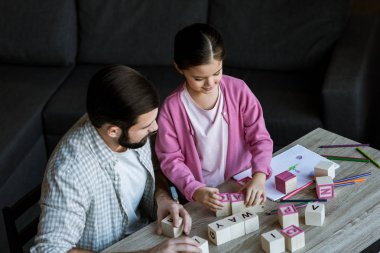 Baba ile kızı masada oturan ve küpleri evde harfleri ile kelime yapma 