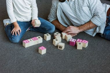 cropped image of father with daughter making words by cubes with letters at home clipart