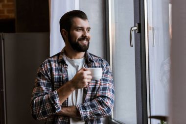 happy handsome man with coffee cup looking at window clipart