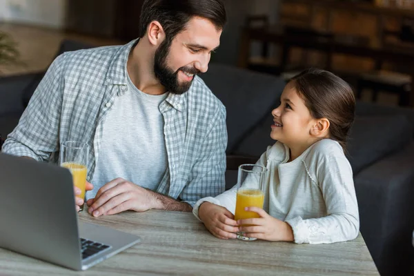 Padre Sonriente Con Hija Sentada Mesa Con Jugo Uso Ordenador — Foto de Stock