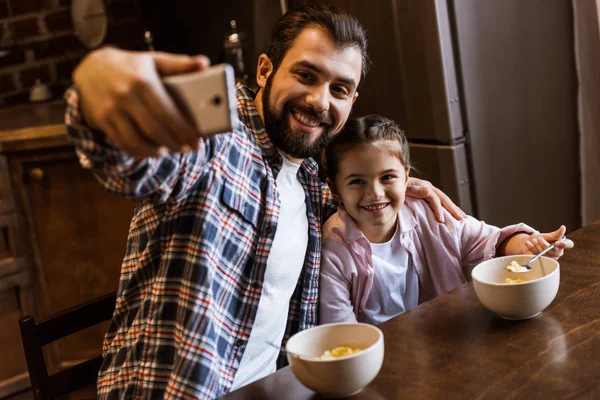Happy Father Daughter Sitting Table Snacks Bowls Takes Selfie Kitchen — Stock Photo, Image