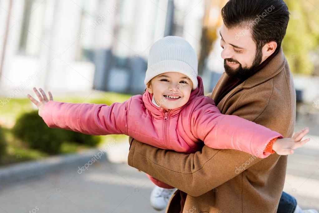 happy father holding her daughter and she making plane. outside