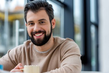 yakışıklı adam kahve hatmi ve kameraya bakarak ile tutarak gülümseyen