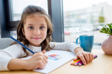 adorable kid holding colored pencil and looking at camera clipart