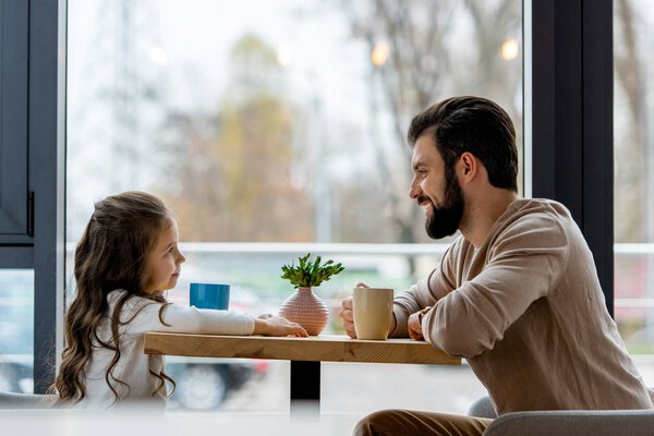 happy father and daughter sitting in cafe and looking at each other 