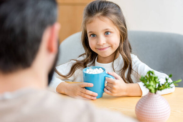cropped image of adorable daughter looking at her father and holding cup of cacao with marshmallow