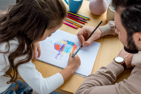 father and daughter sitting at table and drawing in album