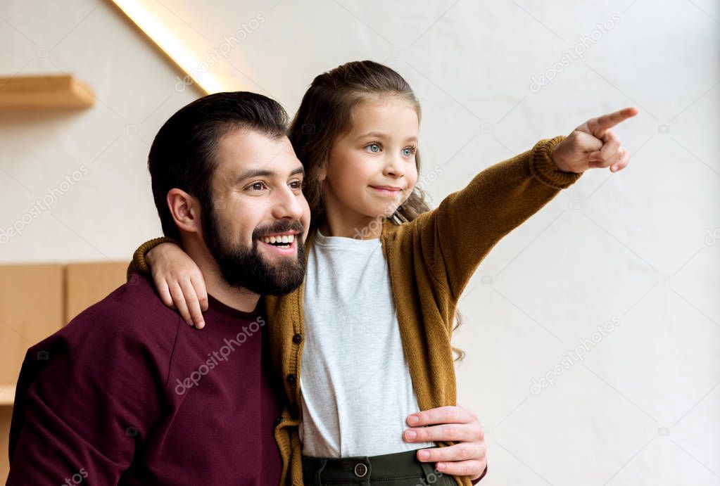 happy daughter pointing on something and hugging father 