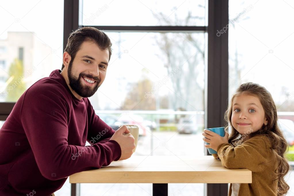 father and daughter holding cups and looking at camera