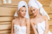 schöne junge Frauen mit Handtüchern bedeckt entspannen sich in der Sauna und schauen in die Kamera