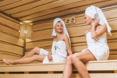 Sauna bankta oturan ve konuşmak güzel genç kadın