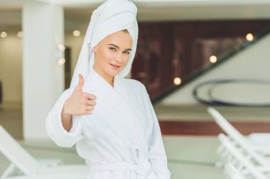 bornoz spa salonu başparmak göstermek yukarıya içinde gülümseyen genç kadın