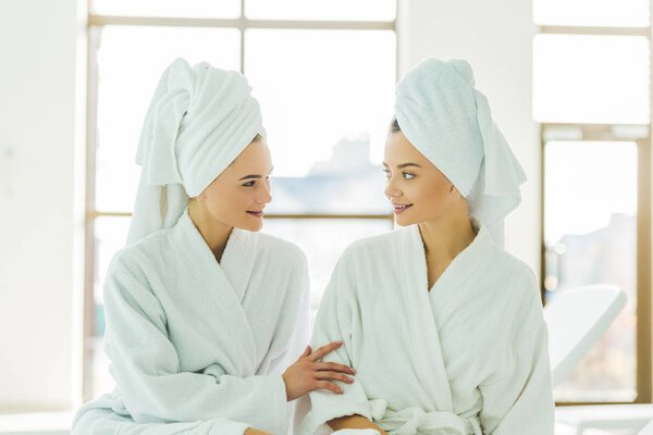beautiful young women in bathrobes and towels on head talking to each other at spa center