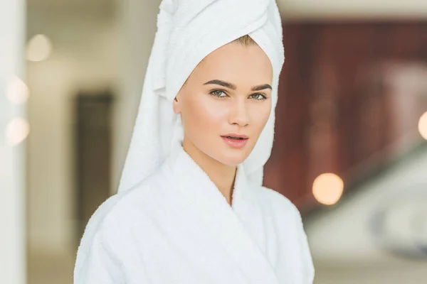 beautiful young woman in bathrobe and towel in spa salon looking at camera