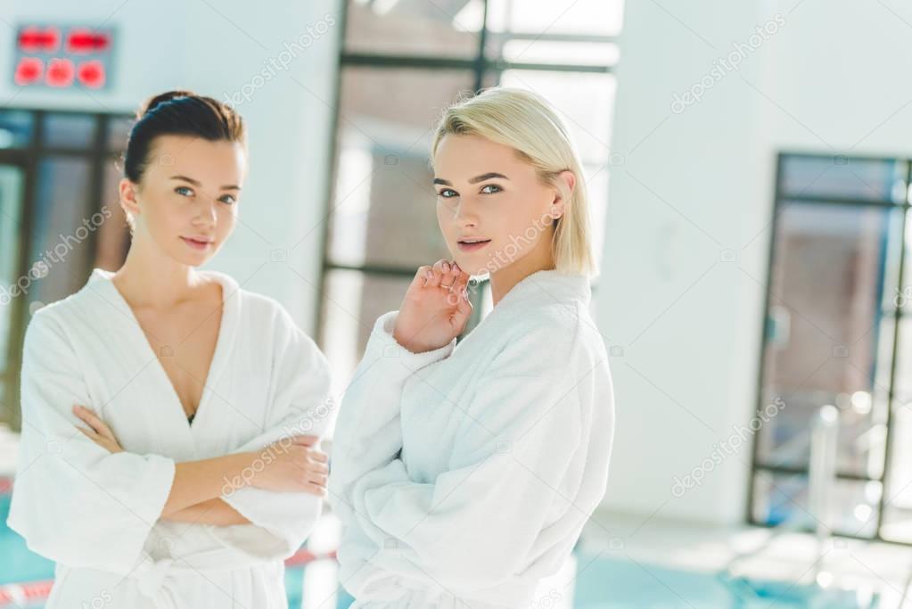 beautiful young women standing in front of swimming pool at spa center and looking at camera