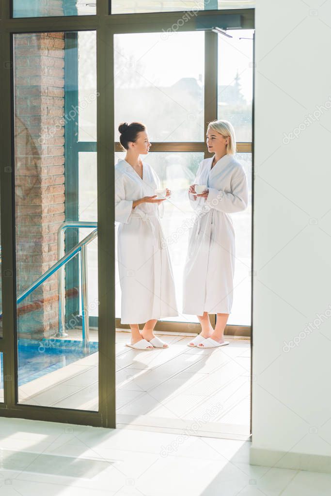beautiful young women in bathrobes drinking coffee at spa center