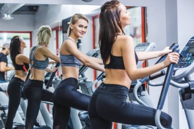 spor salonunda eliptik makineleri üzerinde çalışan genç atletik kadınlar