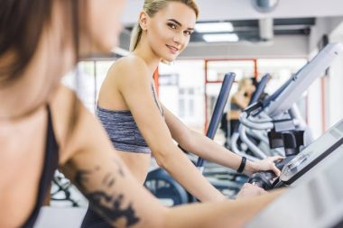 close-up shot of sportive women working out on elliptical machines at gym clipart