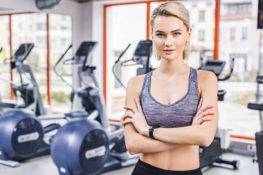 spor salonunda eliptik makineleri önünde çapraz silah ile duran genç çekici kadın