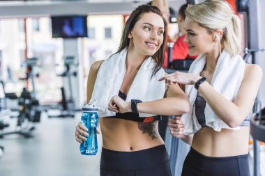 sportive women with towels checking fitnes results with smart watch after training at gym clipart
