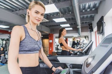 attractive sportive woman running on treadmill at gym with earphones clipart