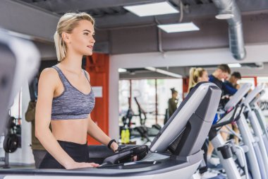sportive young woman running on treadmill at gym clipart
