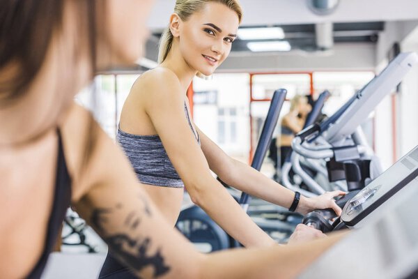 close-up shot of sportive women working out on elliptical machines at gym