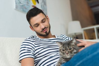 Evcil hayvanlar sevimli tekir kedi kanepede otururken yakışıklı genç adam