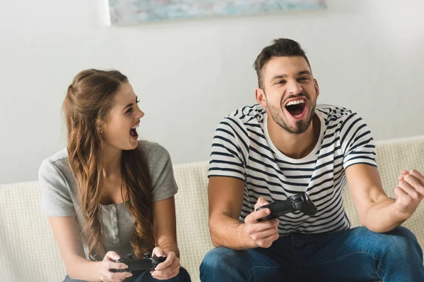 happy young couple playing games with gamepads at home