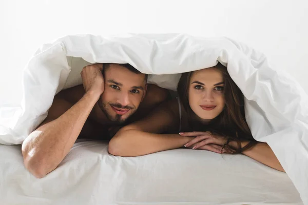 Joven Pareja Bajo Manta Mirando Cámara Cama — Foto de Stock