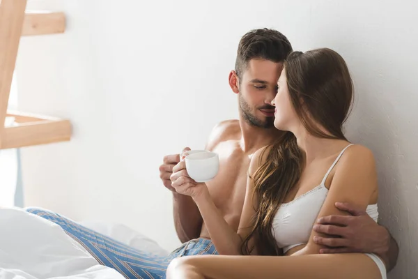 ベッドで朝のコーヒーを飲みながら下着で美しい若いカップル — ストック写真