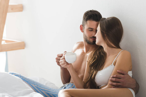 beautiful young couple in underwear drinking coffee in bed in morning
