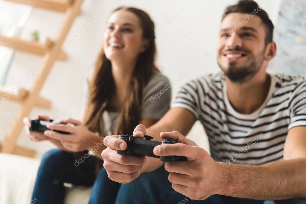 smiling young couple playing games with gamepads at home