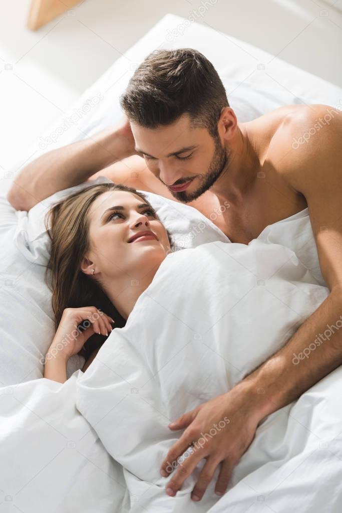 smiling young man embracing girlfriend from behind in bed in morning