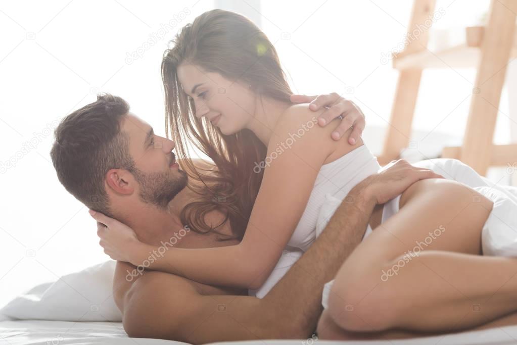 smiling young couple in underwear embracing in bed at sunny morning