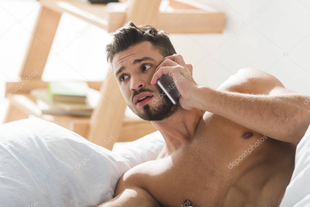 shocked overslept man talking by phone in bed in morning