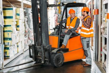 two male workers using forklift machine in storehouse clipart