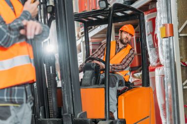Emanet yelek ve kask içinde forklift makine depolama içinde oturan işçi