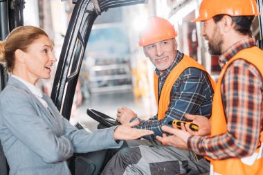 üst düzey alt Emanet yelek ve kask içinde forklift makine oturan ve depolama birimindeki arkadaşları ile konuşurken