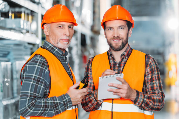 two male workers holding walkie talkie and notepad in storehouse