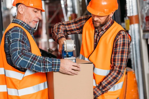 Manliga Arbetstagare Säkerhets Västar Och Hjälmar Packning Kartong Med Tejp — Stockfoto